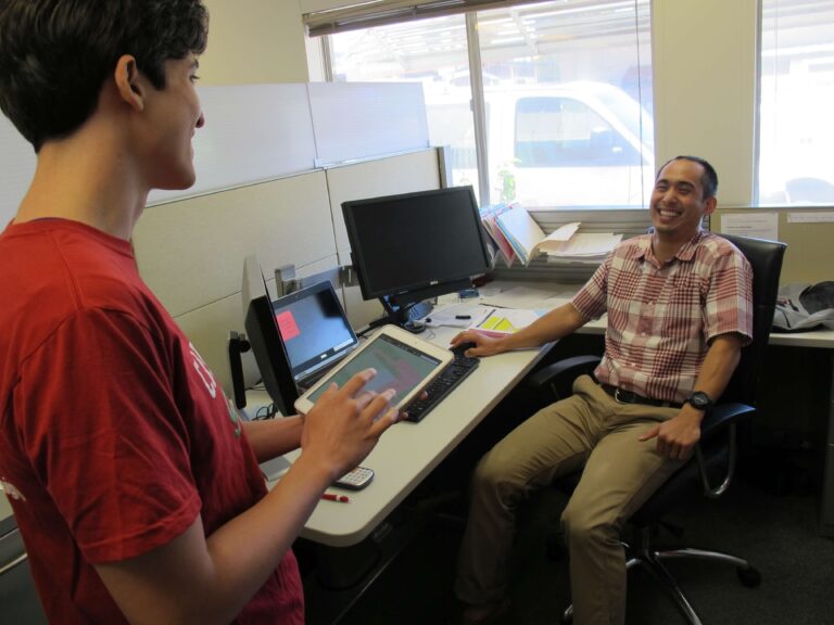 Student and teacher in teacher office laughing while student is holding tablet