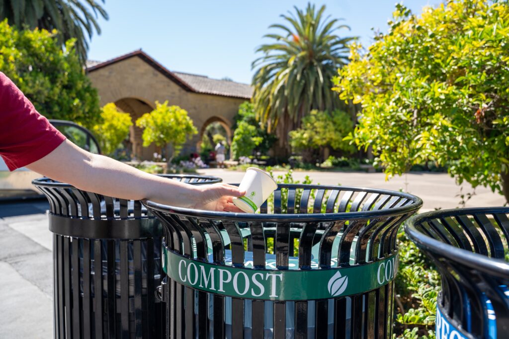 Person throwing a compostable cup into a compost bin outside