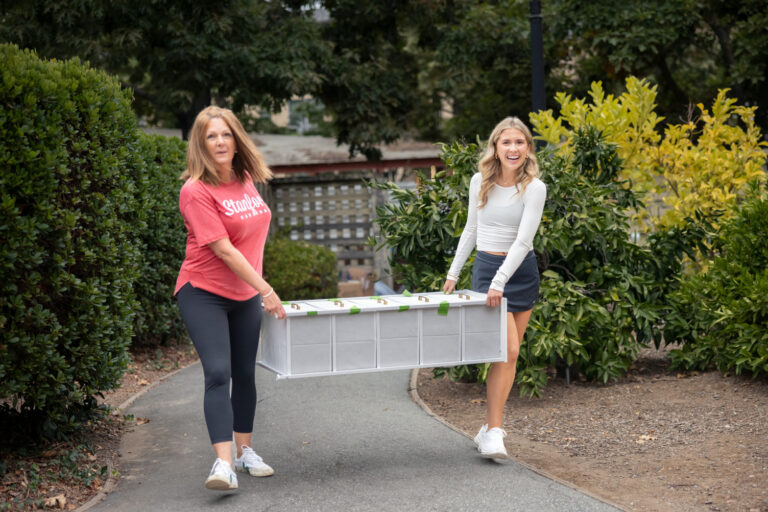 Mother and daughter carrying a shelving unit as they move into campus