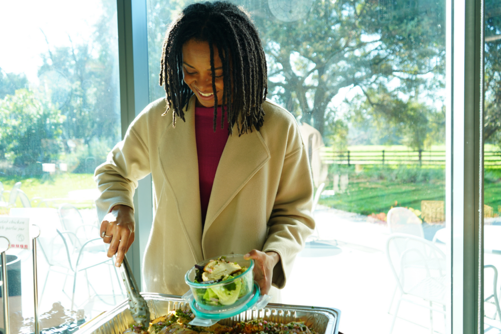 Woman smiling placing food into a glass reusable container.
