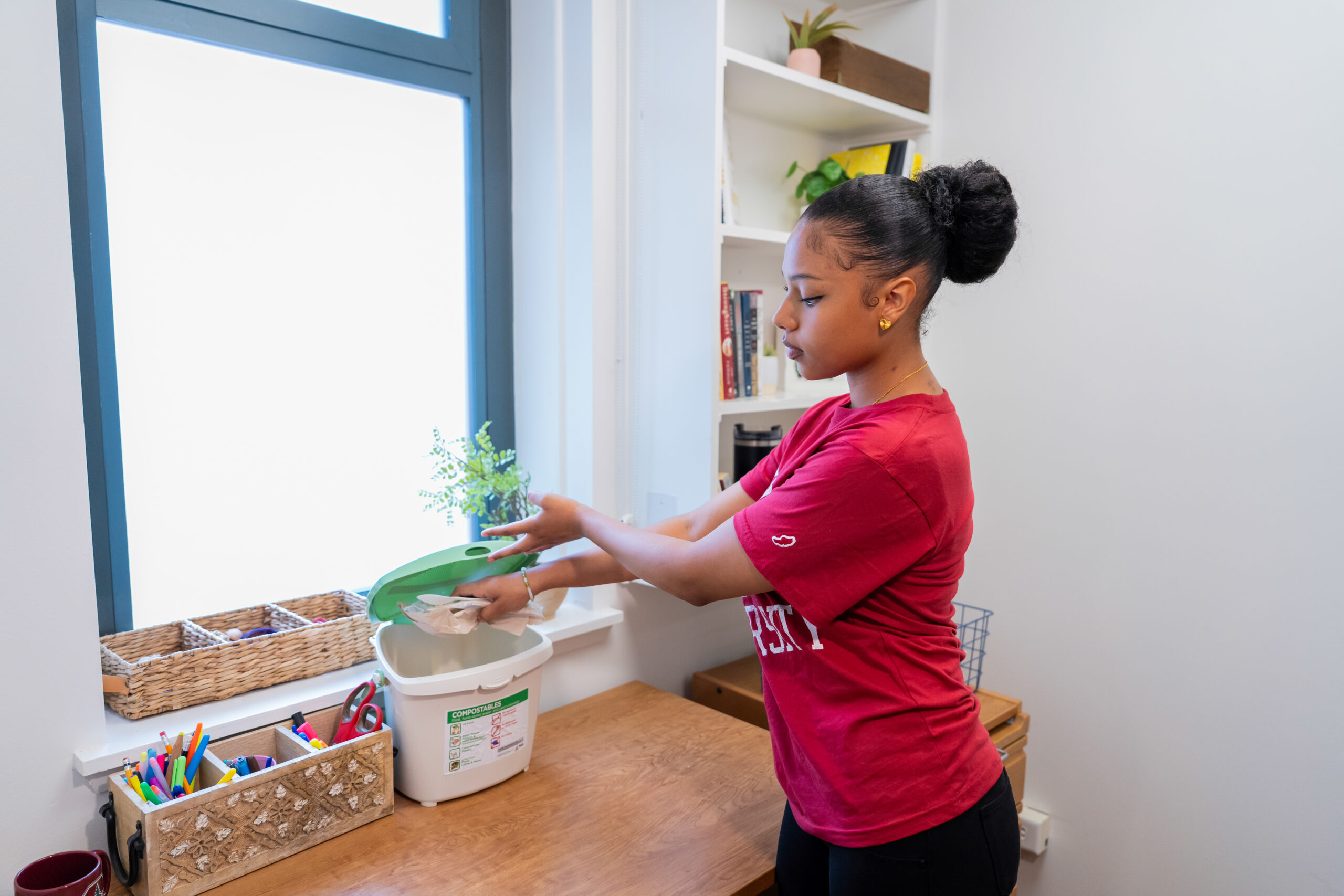 Student placing a paper towel in a compost bin inside her dorm room. sustainability habits in their dorm room. 