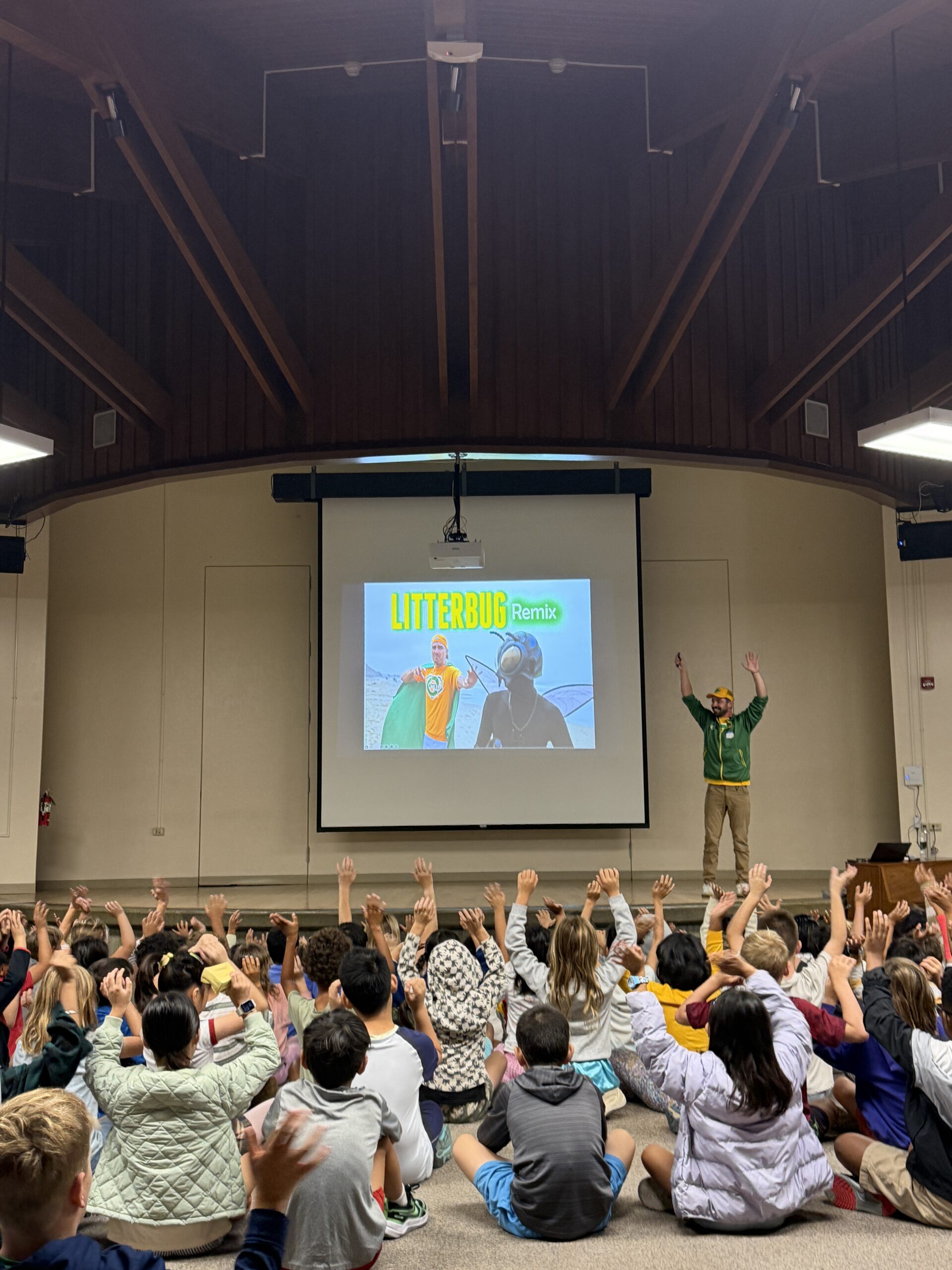 Students in front of a stage with their hands in the air. The screen reads "Litterbug Remix"
